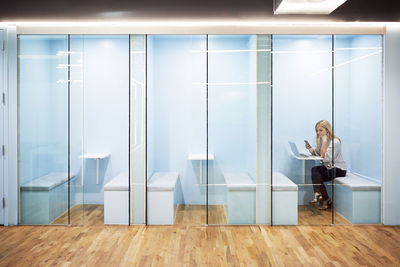 Businesswoman using laptop and mobile phone while sitting in cubicle at creative office