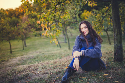 Beautiful brunette in a knit sweater sitting under the tree in an autumn park