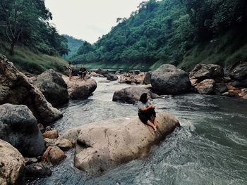 Man on rocks by river against mountains