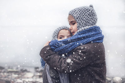 Cute smiling siblings embracing by lake during winter