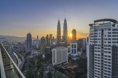 Petronas towers amidst buildings against sky during sunset