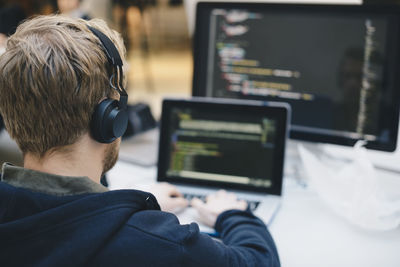 Over the shoulder view of businessman wearing headphones while programming on laptop at creative office