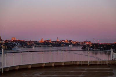 Illuminated buildings by river against sky during sunset