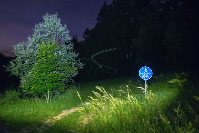 Road sign on field by trees at night