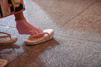 Low section of girl putting slippers while standing on floor