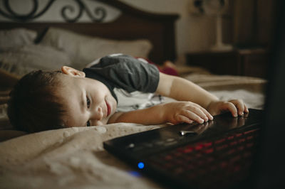 Boy lying on bed and using laptop at home