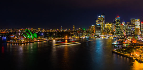 Illuminated buildings by river against sky at night