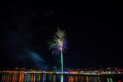 Firework display over illuminated city against sky at night