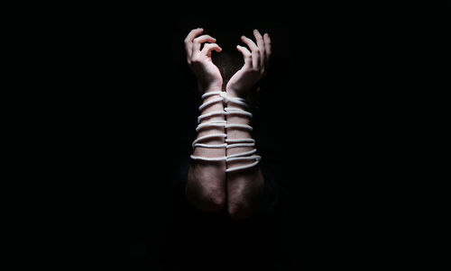 Close-up of cropped hand of man tide with rope against black background