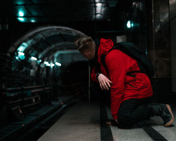 Side view of man kneeling at illuminated railroad station platform