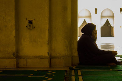 Side view of woman sitting against wall in building