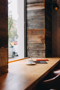 Coffee cup and laptop sitting on a table by a window in a coffee shop