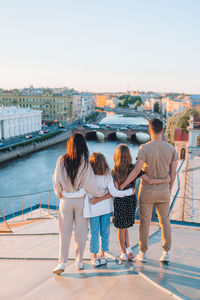 Rear view of women standing on shore against cityscape