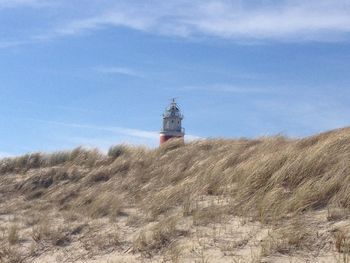 Lighthouse on field by building against sky