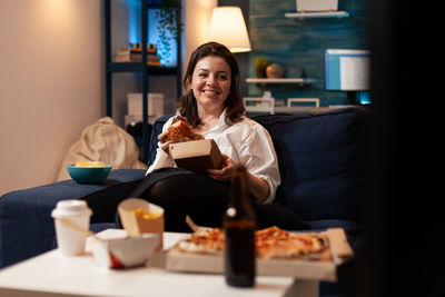 Smiling woman eating food while sitting at home