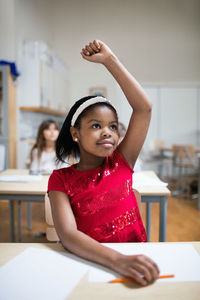 Concentrated girl with hand raised sitting at desk in classroom