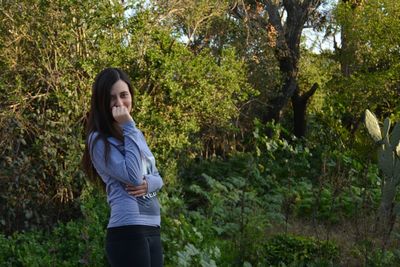 Portrait of young woman standing against trees