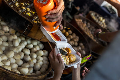 Cropped image of vendor pouring sauce in container held by child