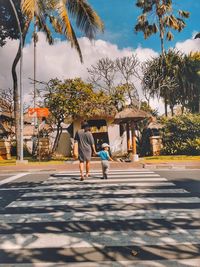 Rear view of people walking on palm trees against sky