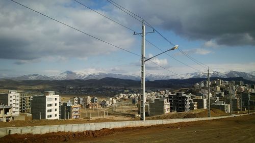 Electricity pylon by buildings in city against sky