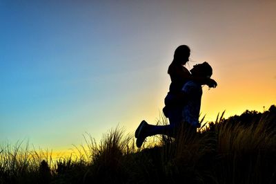 Silhouette couple on field against sky during sunset