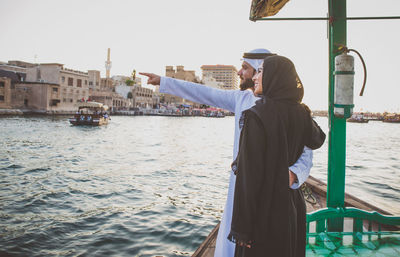 Smiling couple looking at view while standing in boat on river during sunset