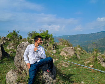 Side view of woman sitting on rock against sky