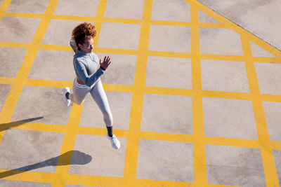 From above of determined female jogger in activewear running on pavement with ornament and shadow in sunlight