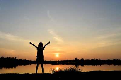 Silhouette person standing by lake against sky during sunset