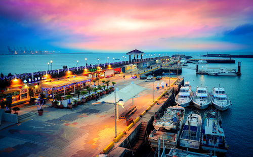 High angle view of illuminated city by sea at sunset