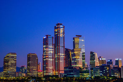 Illuminated modern buildings against clear blue sky