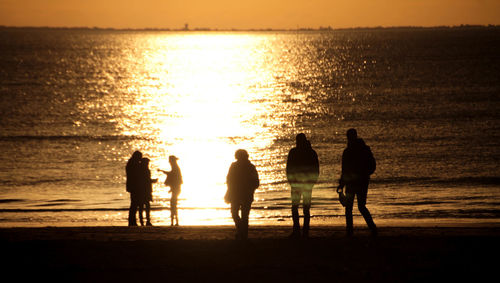 Silhouette of people standing on beach at sunset