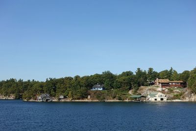 Scenic view of river by trees against clear blue sky