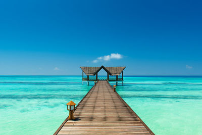 Pier over sea against clear blue sky