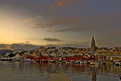 Scenic view of river by buildings against sky at sunset