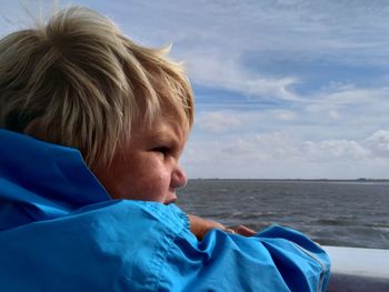 Portrait of boy relaxing by sea against blue sky