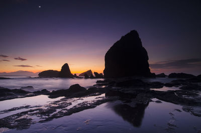 Silhouette rock formation in sea against clear sky during sunset