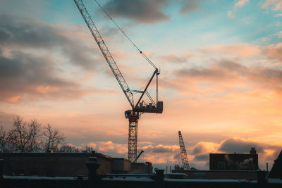 Silhouette cranes at construction site against sky during sunset