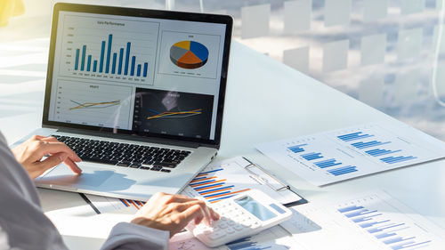 Cropped hands of businesswoman using laptop and calculator at office