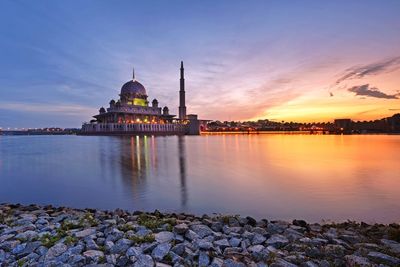 Silhouette mosque by lake against sky during sunset