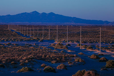Electric power poles cables, high voltage, row towards, landscape valley, sand, dirt road, sunset,