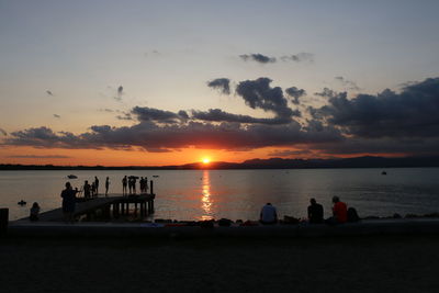 Silhouette people on beach against sky during sunset