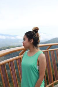 Young woman looking away while standing against railing