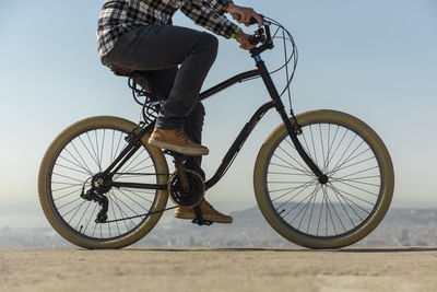 Low section of man riding bicycle on retaining wall against clear blue sky during sunny day