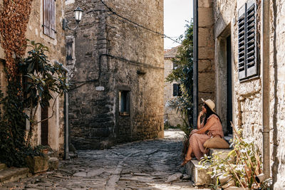Young woman in pink dress sitting in street of old town, picturesque, alone, travel, one person.