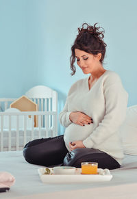 Young woman looking at camera while sitting on wall at home