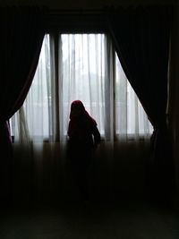 Rear view of woman looking through window at home