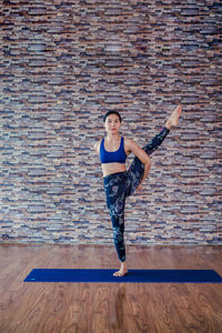 Full length of woman practicing yoga against wall