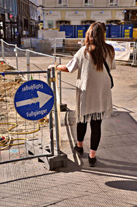 Rear view of woman standing by directional sign on road in city