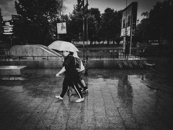 Woman with umbrella walking on wet street during rainy season